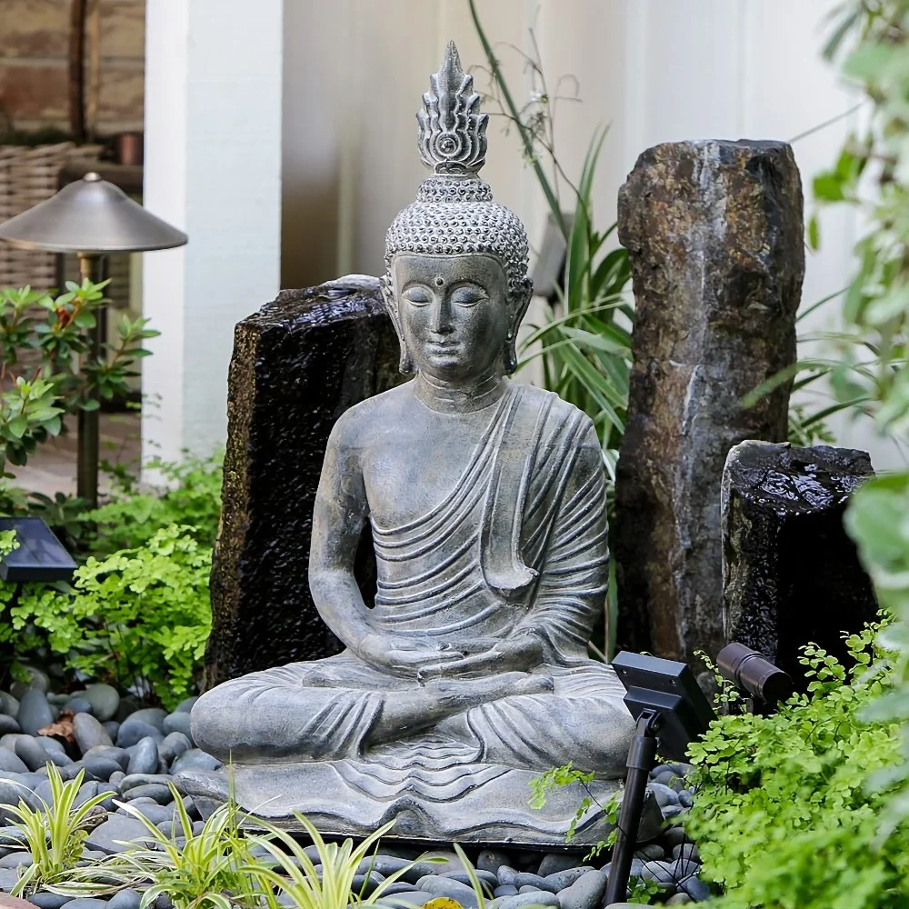 A Buddha statue sitting in a peaceful garden surrounded by rocks, plants, and stone water features.