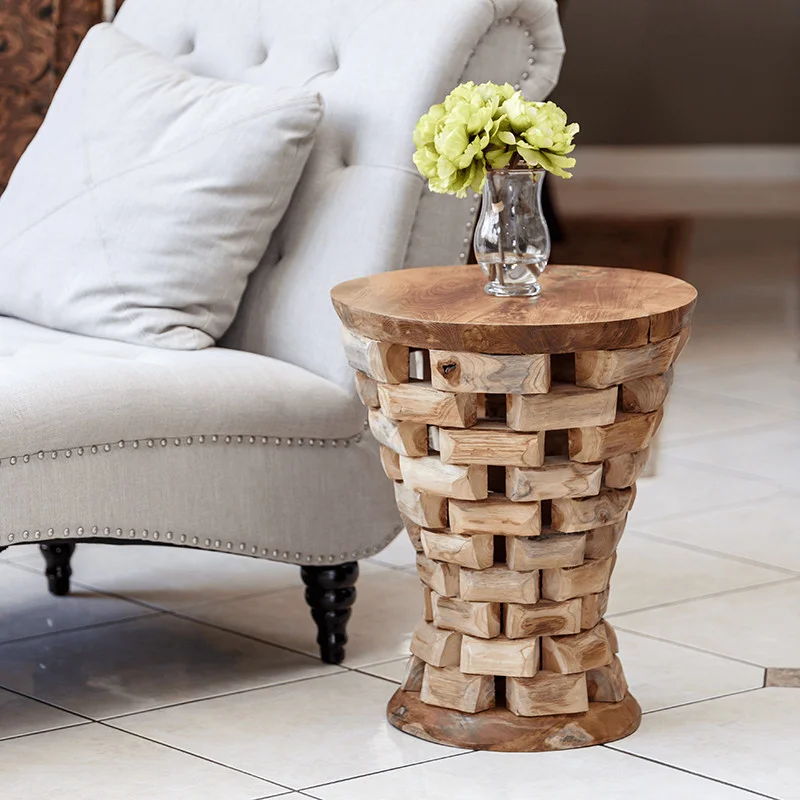 A rustic wooden side table made from stacked wood pieces, placed beside a white upholstered chair in a cozy interior.