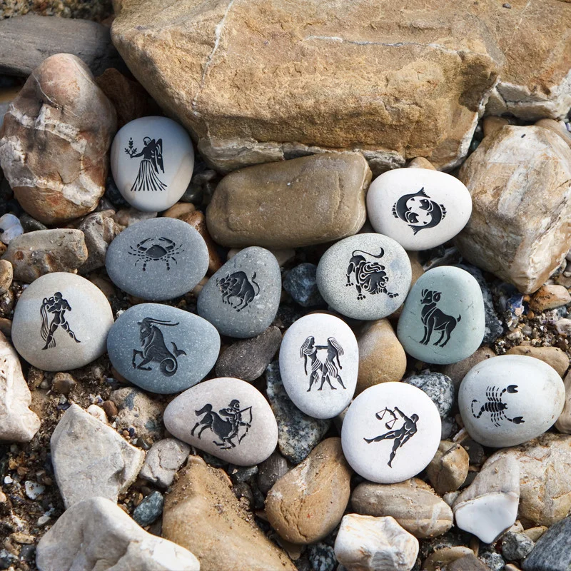 Decorative stones painted with zodiac symbols, arranged among natural rocks and pebbles.